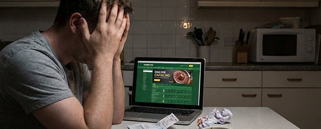 Mann mit Händen vor Gesicht neben Laptop mit Glücksspiel